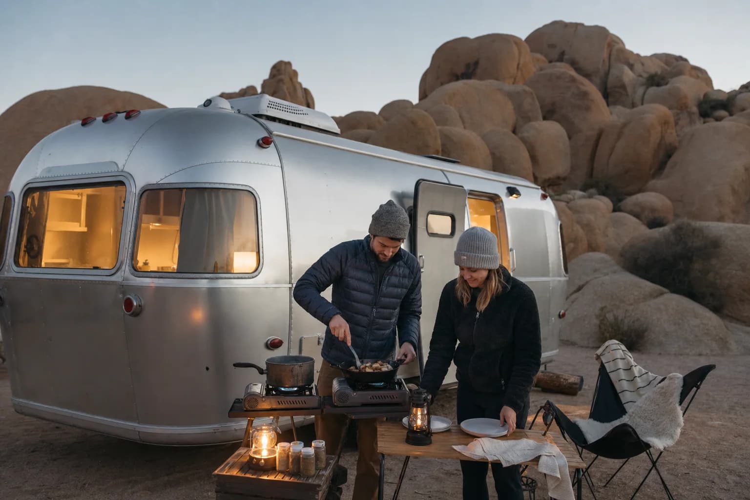 Dana and Malik cook an anniversary dinner beside their aluminum trailer among Joshua Tree boulders